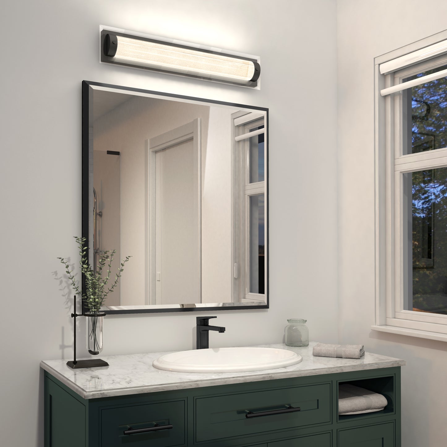 Modern bathroom with a green vanity, white marble countertop, rectangular mirror, black faucet, glass jar, small towel, and the Artika Glamour LED bathroom vanity light 3 CCT above the mirror. Natural light enters through a window.