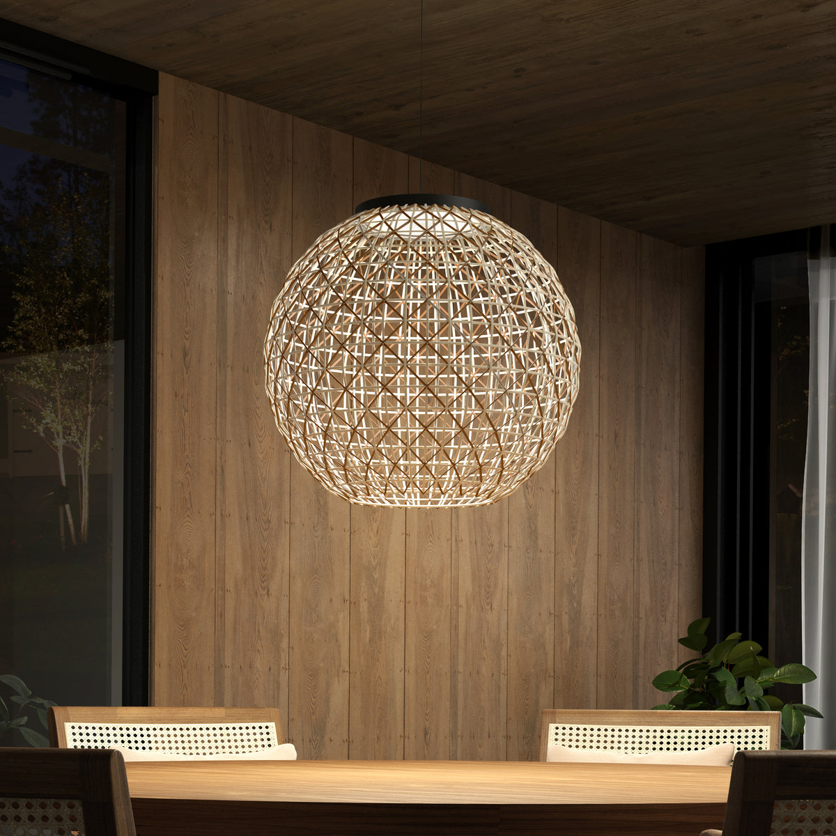 The Artika Benson LED pendant light 5 CCT hangs above a wooden dining table with chairs in a modern room featuring wood-paneled walls, large windows, and a potted plant in the corner.