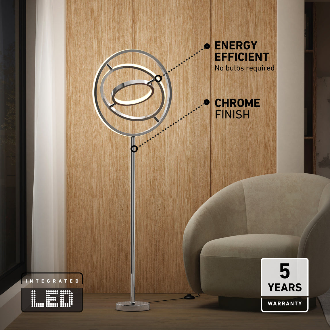 The Artika Pivot modern LED floor lamp 3 CCT with a sleek chrome finish and circular LED rings stands by a beige armchair and wood-paneled wall. Features include energy efficiency, integrated LED, and a 5-year warranty.