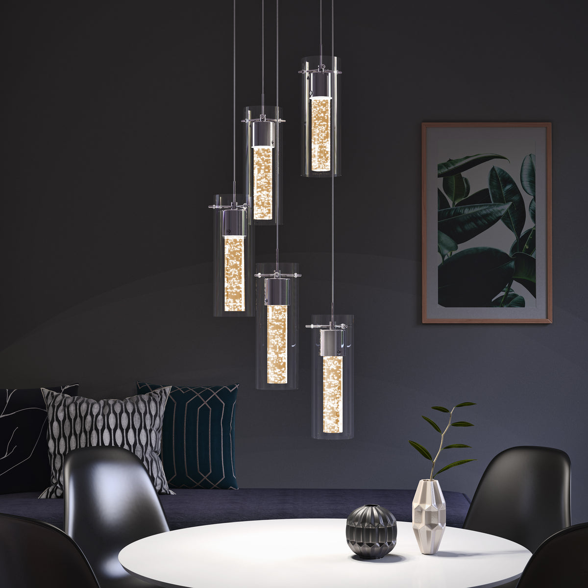 Modern dining room featuring an Artika Essence 5-light LED pendant above a round white table with black chairs. A dark sofa with patterned cushions and a framed leafy art print complete the background.