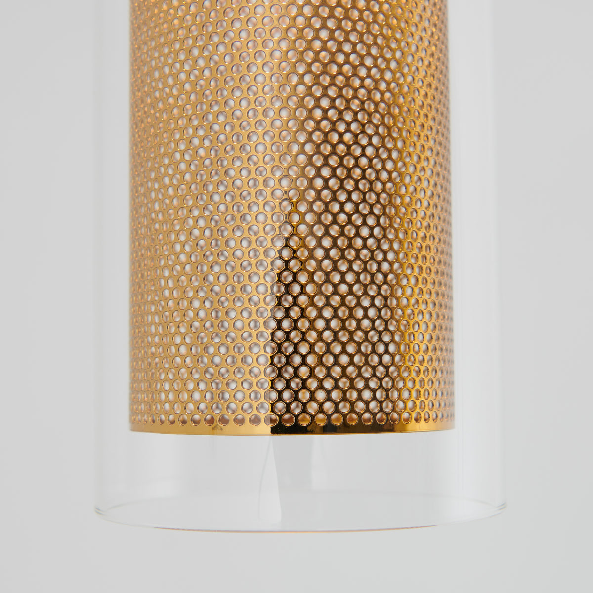 Close-up of Artika’s Oxion 1-light LED pendant: a cylindrical fixture featuring a perforated metallic gold interior encased in clear glass, shown against a plain light gray background.