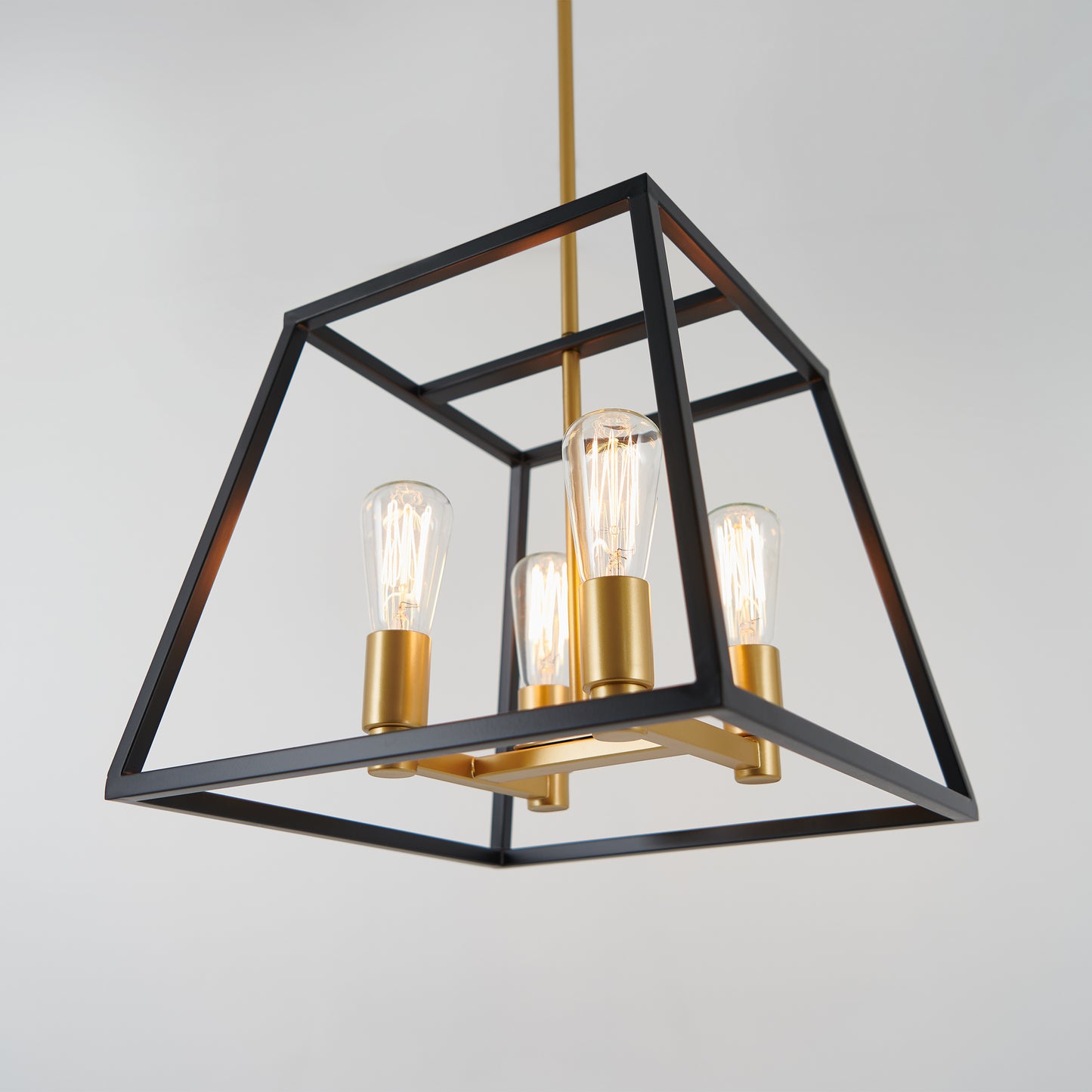 The Carter Square 4-light Chandelier by Artika features exposed bulbs, gold sockets, and a geometric black metal frame, hanging elegantly from the ceiling against a plain white background.
