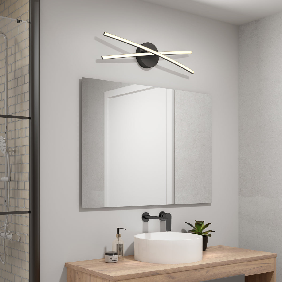 Modern bathroom with a large mirror, wooden countertop, white sink, black faucet, and potted plant. Above the mirror is the Artika Orly 25-in Modern Integrated LED 3-CCT Vanity Light, enhancing the contemporary decor. Shower area partially visible.