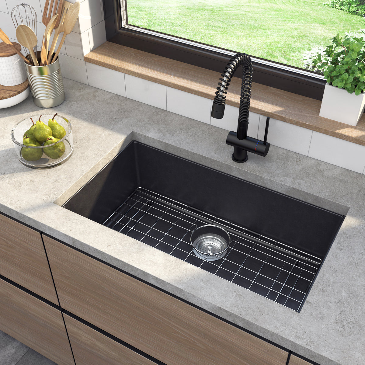 Artika Baycrest 33 in. black kitchen sink with black faucet, metal rack, utensils, pears in bowl, plant, and yard view window.