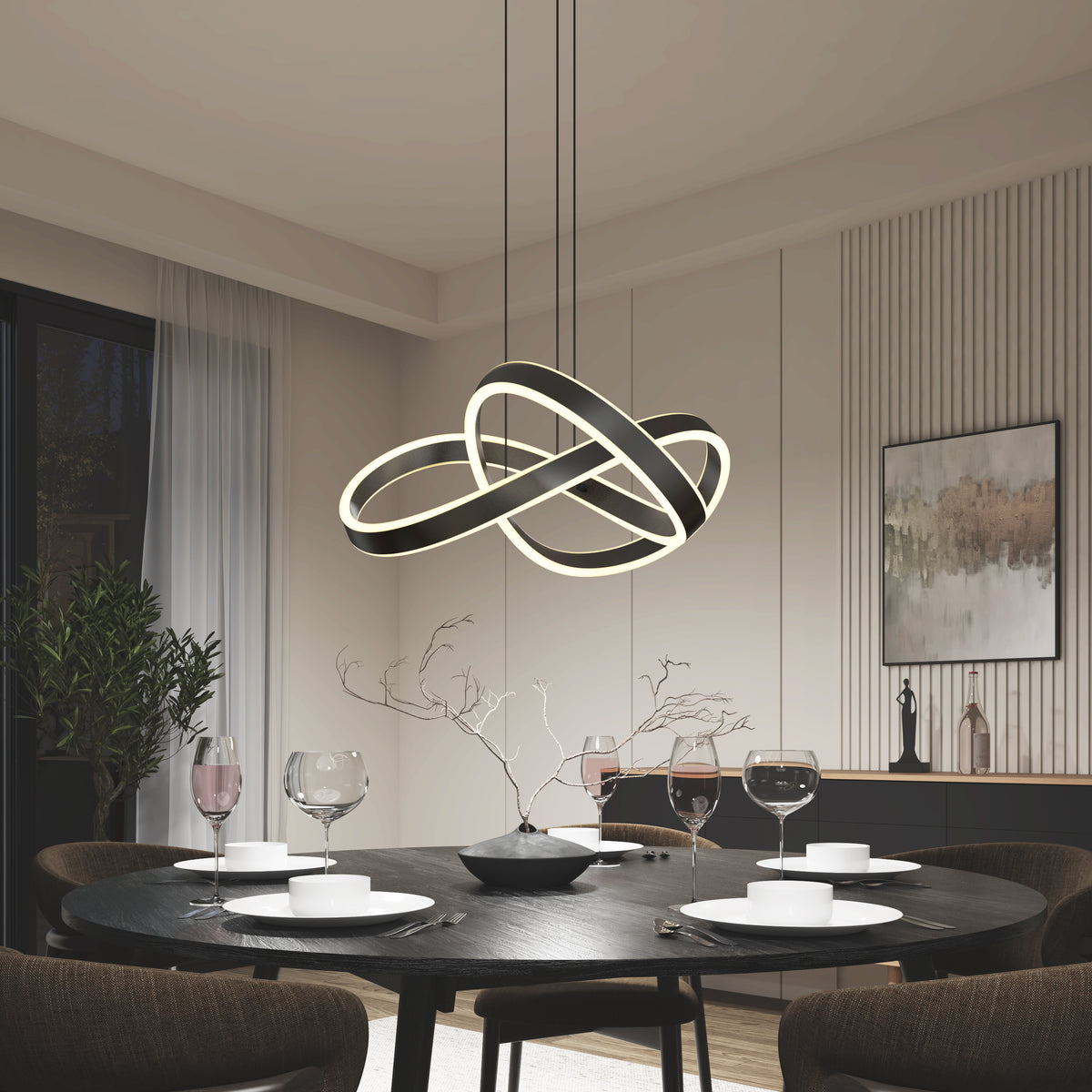 A modern dining room with a round black table set for four, featuring white plates, wine glasses, a minimalist branch centerpiece, and the sculptural Bolero LED pendant light by Artika hanging above. Contemporary art and plants decorate the space.