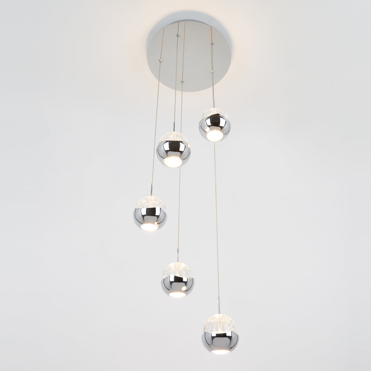 The Artika Oracle modern 5-light LED pendant features five chrome-finished spheres hanging at varying lengths, casting white light against a plain white background.
