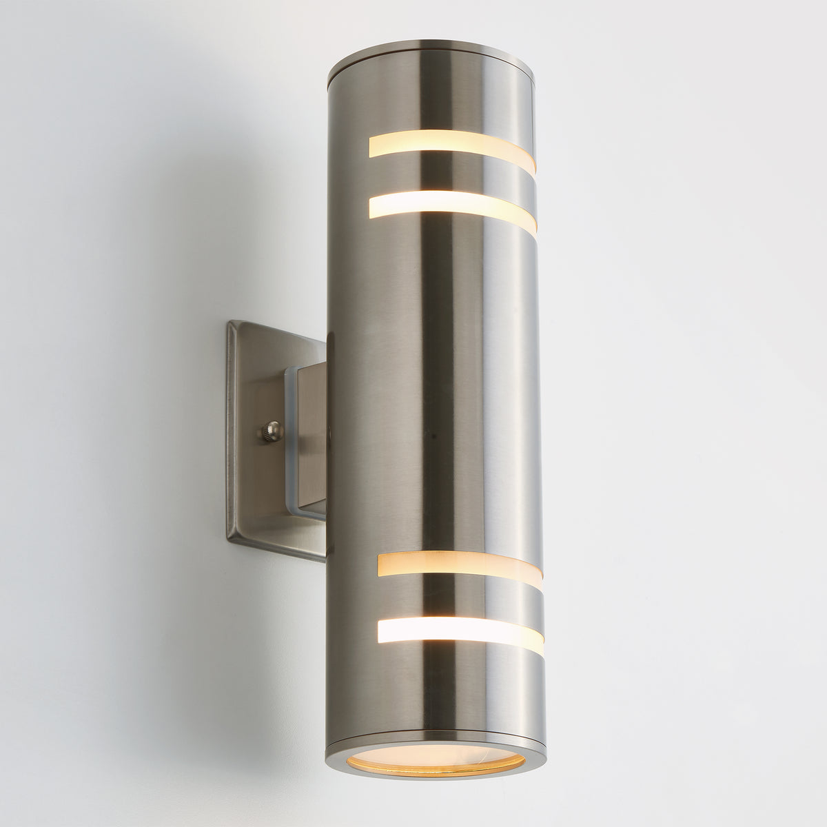 The Artika Voltz indoor-outdoor wall light features a modern cylindrical brushed metal design with horizontal cutouts, mounted on a square plate against a plain white background.