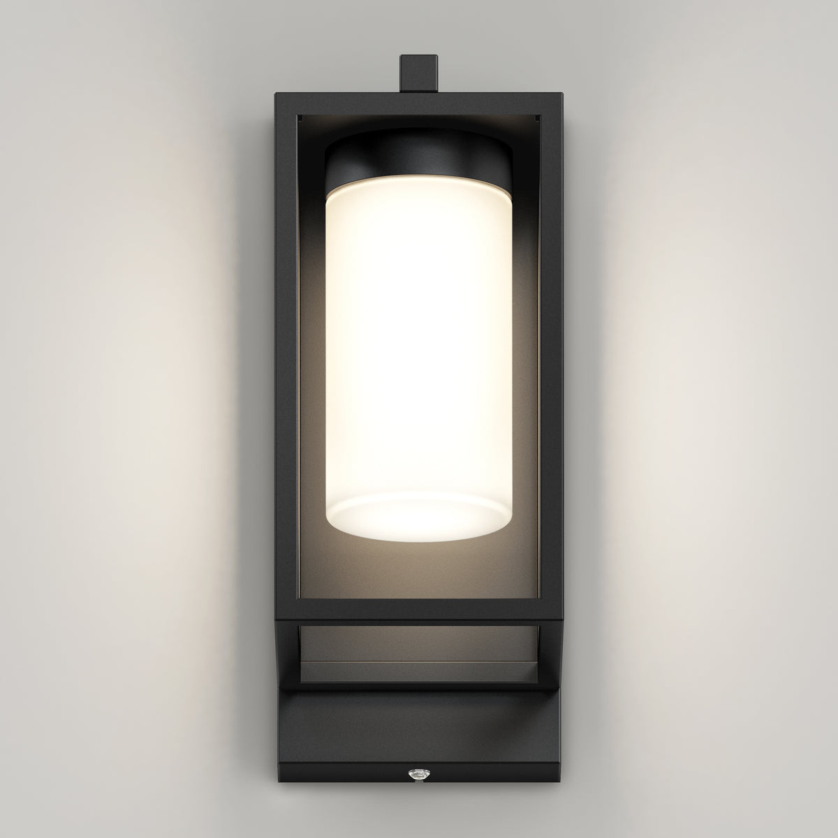 The Artika Aurel Outdoor LED Light, 3CCT, features a modern black rectangular frame with a cylindrical frosted glass fixture, mounted on a light gray wall and emitting a soft, even glow.
