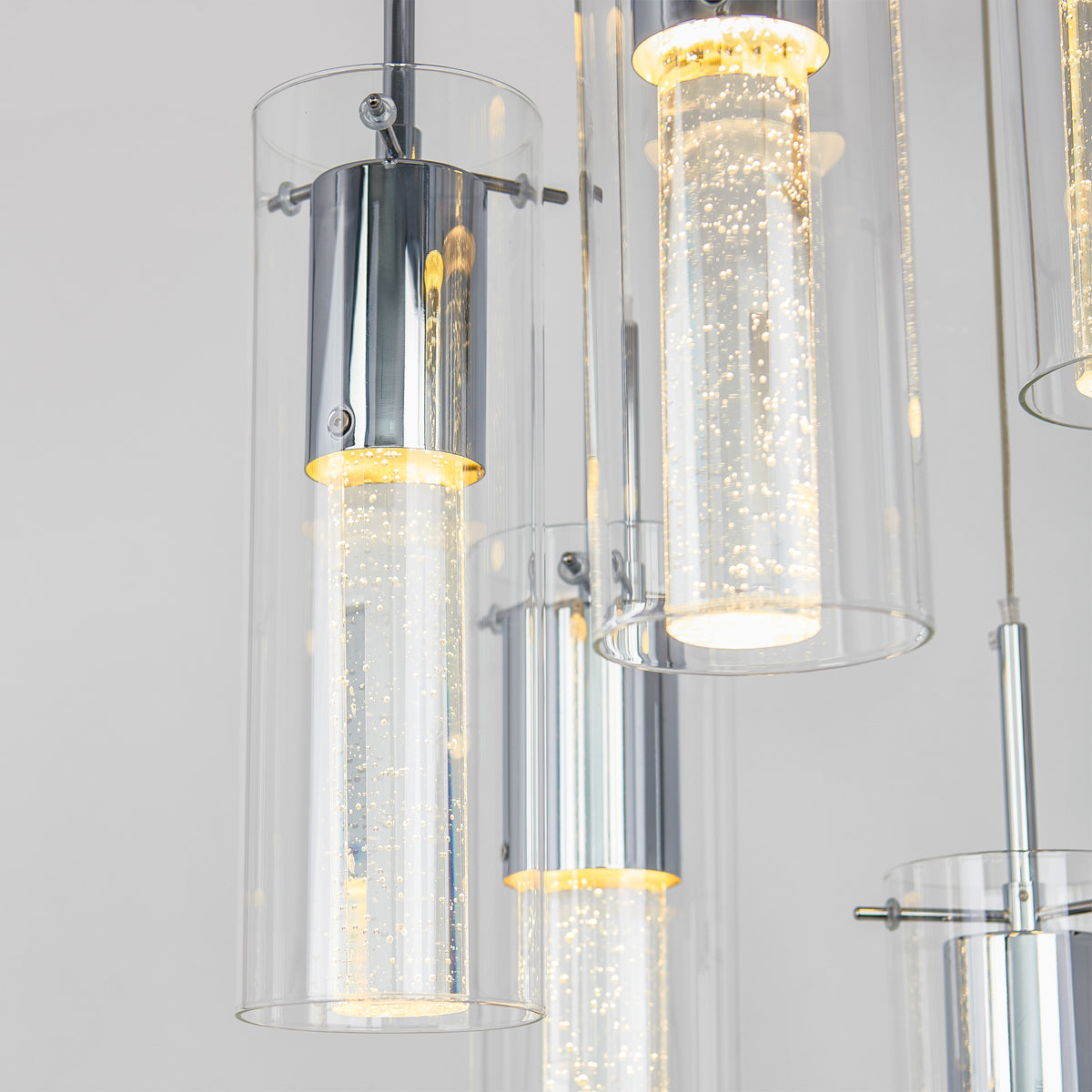 Close-up of the Artika Essence 5-light LED pendant, featuring cylindrical glass shades with bubble-filled inner tubes that emit a warm glow against a plain light background.
