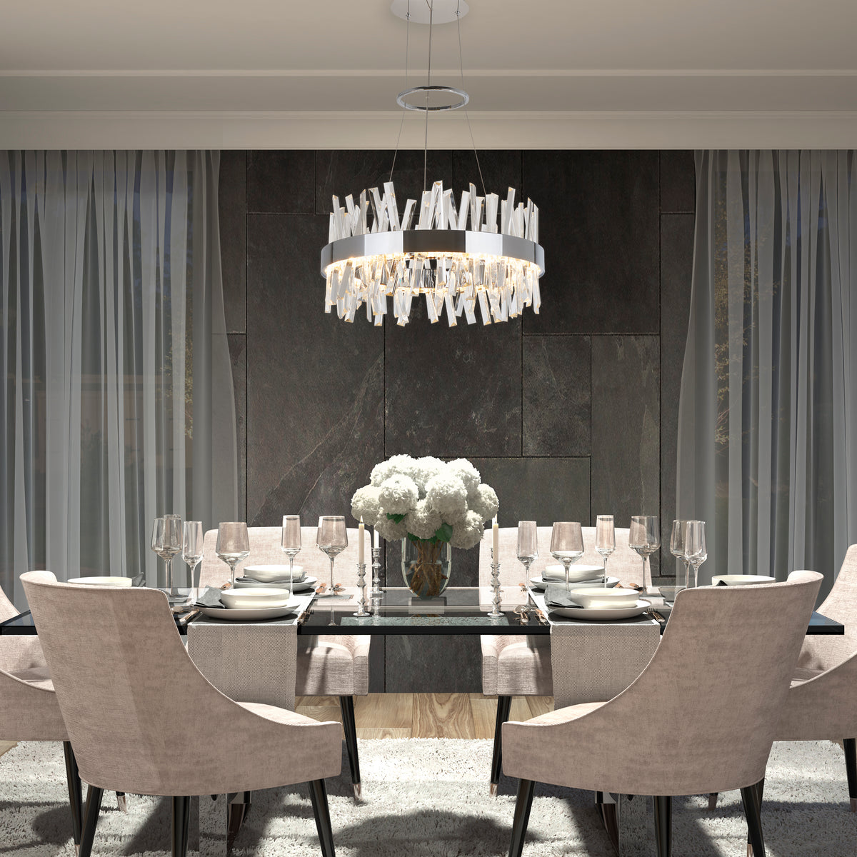A modern dining room features a glass table for six, beige upholstered chairs, a white flower centerpiece, Artikas Enchanted LED pendant light, and floor-to-ceiling curtains against dark stone walls.