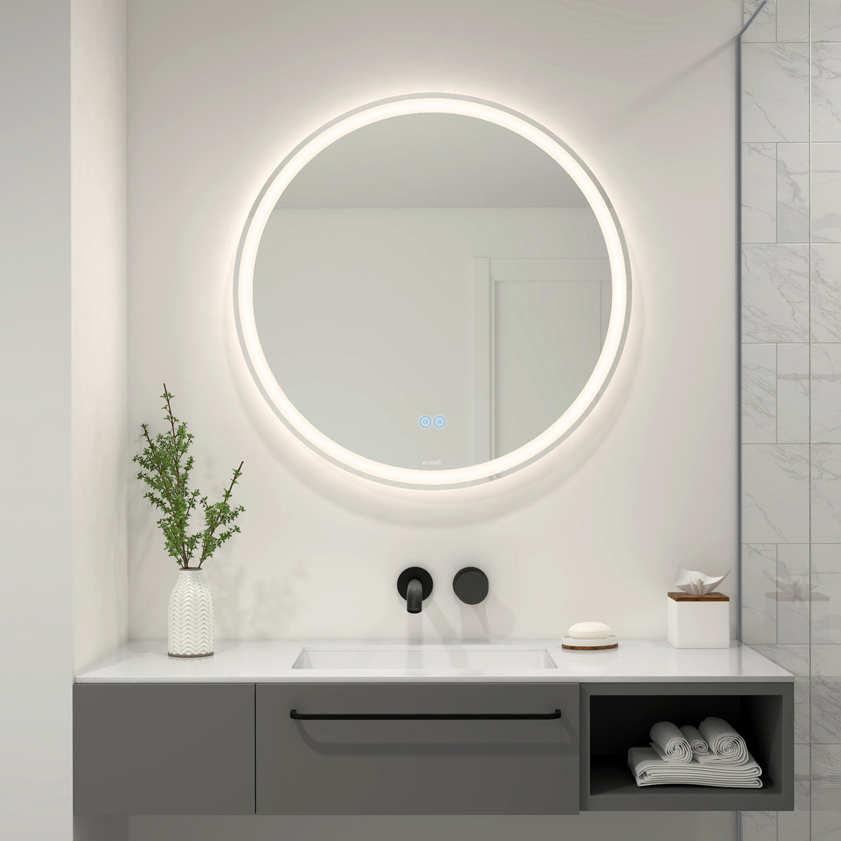 A modern bathroom features the Ayla 28 in. LED mirror 3 CCT with defogger by Artika above a sleek gray vanity. On the counter are a vase with greenery, a soap dish, and tissues. The wall is partly tiled with marble.