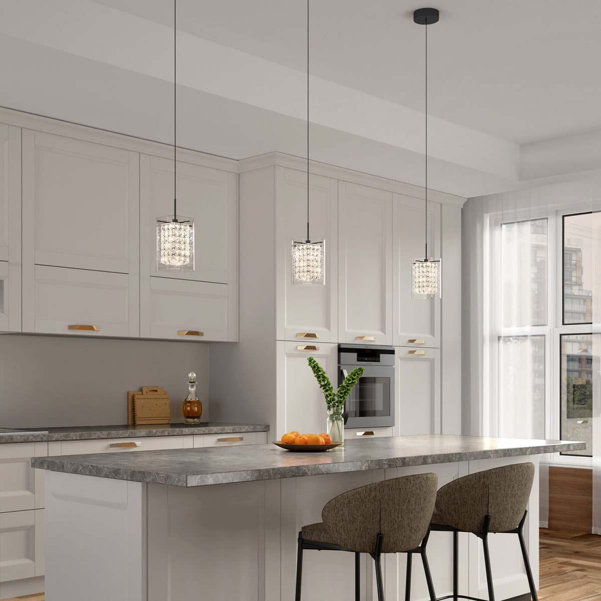 Modern kitchen with white cabinets, a large island featuring a gray marble countertop, two cushioned bar stools, three Artika Crystal Cube 1-light LED pendant lights, a vase with green leaves, and a bowl of oranges on the counter.