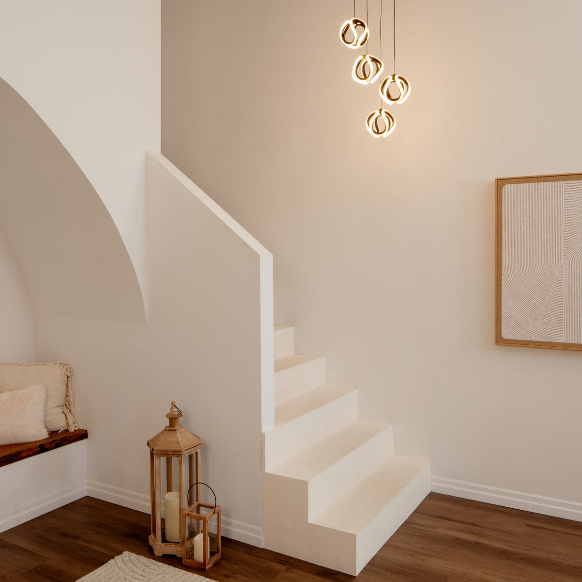 A minimal, modern stairway in a neutral room with white walls, wood floors, abstract wall art, decorative lanterns by the stairs, and an Artika Vivaldi modern LED 4-light pendant illuminating the space.