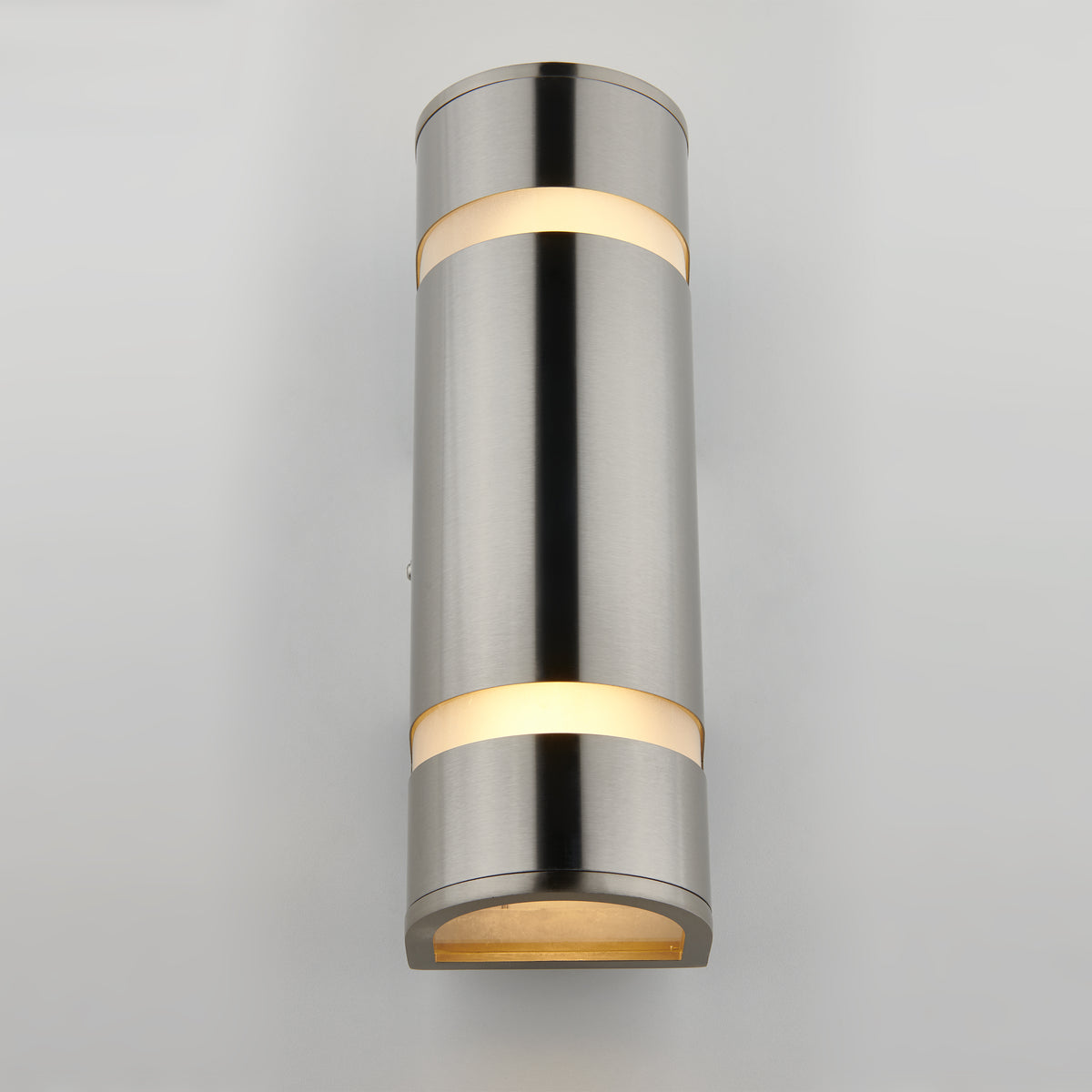 The Artika Q1 indoor-outdoor wall light is a modern cylindrical sconce with a brushed metal finish, casting warm light from the top, middle, and bottom, shown here mounted on a light gray wall.