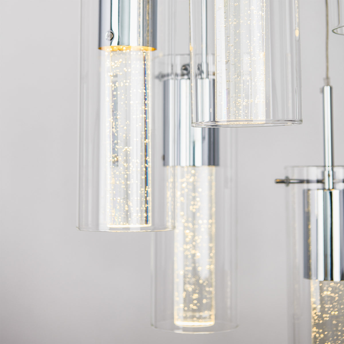 Close-up of the Artika Essence 5-light LED pendant, featuring modern cylindrical glass tubes with chrome finishes and illuminated bubbles inside, set against a neutral background.