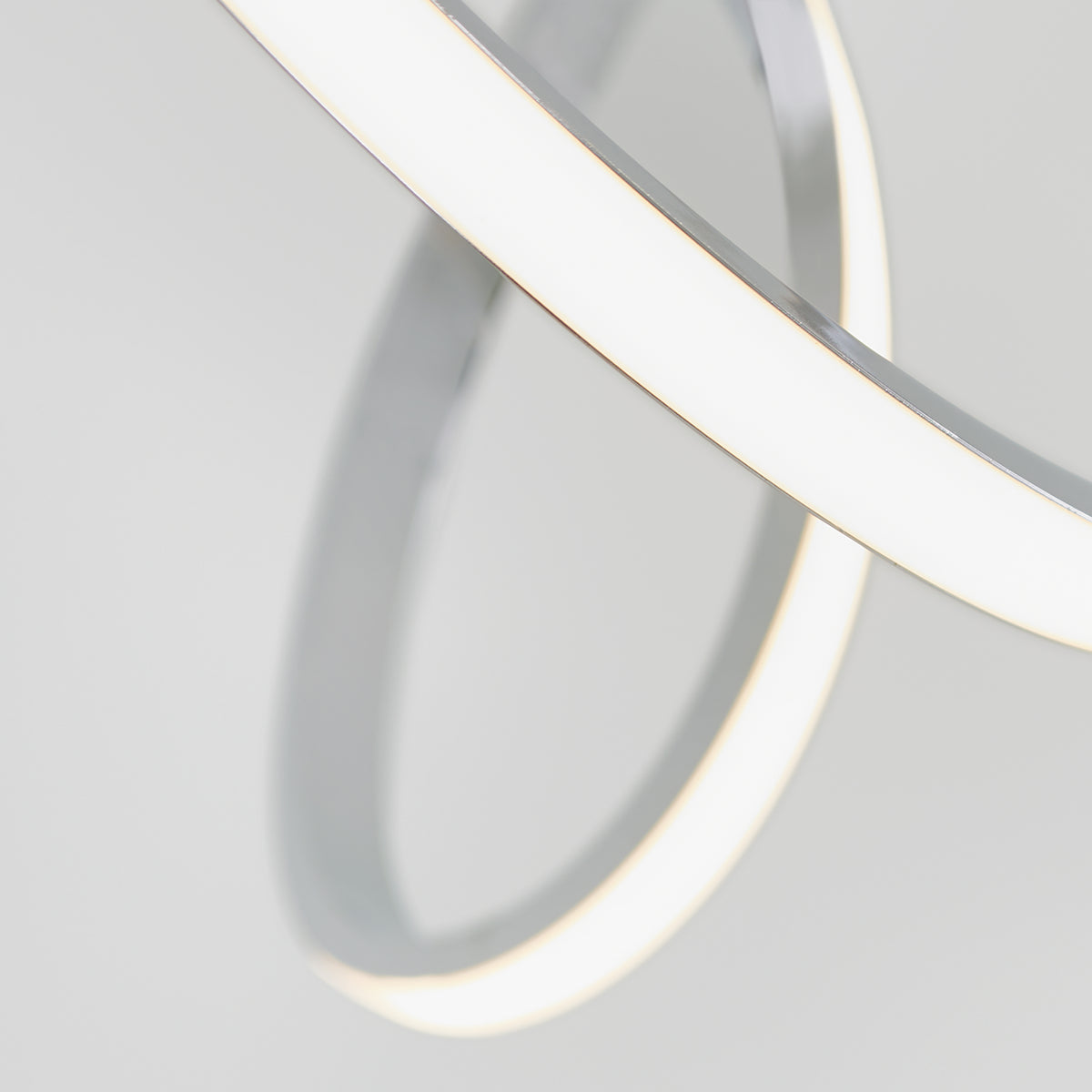 Close-up of two intersecting Swirl LED pendant lights by Artika, featuring curved white and metallic forms against a plain light gray background for a minimalist, modern look.