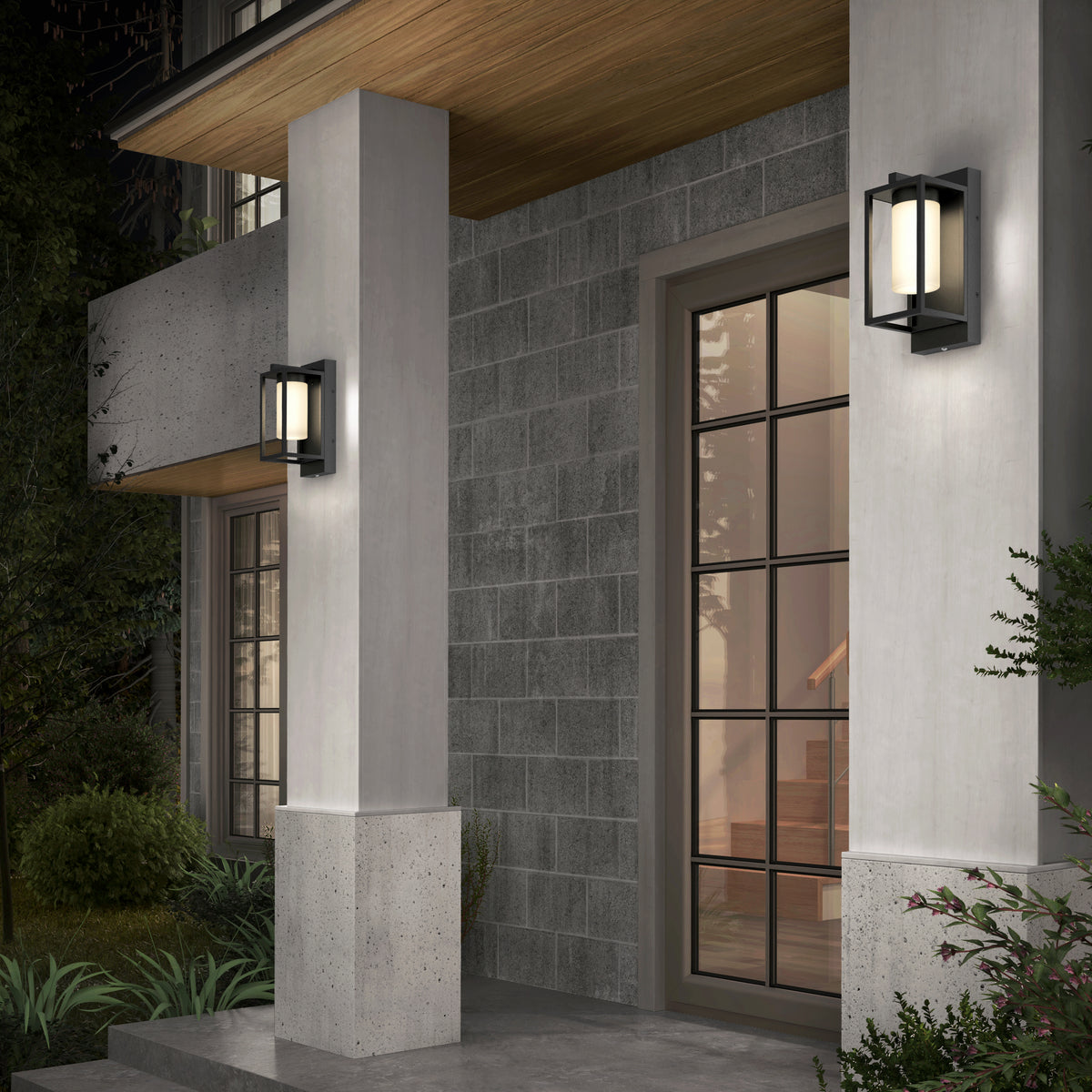 A modern home entrance features gray stone walls, a glass-paneled door, concrete pillars under a wooden ceiling, and two Artika Aurel Outdoor LED Light 3CCT wall fixtures. Steps can be seen inside through the door.