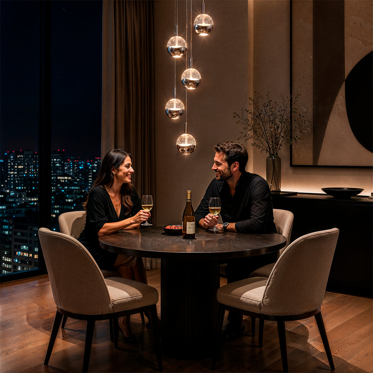 A couple enjoys wine at a round table under an Artika Oracle modern 5-light LED pendant, city lights twinkling outside.