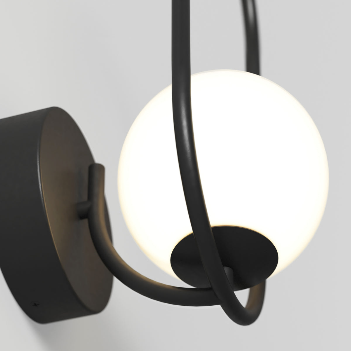 Close-up of the Artika Bloom LED Sconce 3 CCT, featuring a black metal fixture and a round white frosted glass globe that emits soft light, mounted on a light gray wall.
