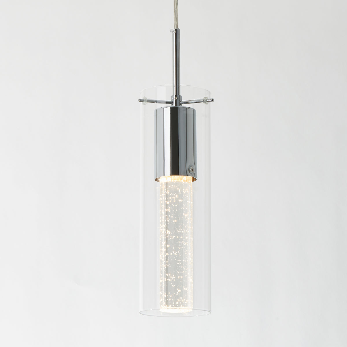 The Artika Bubble Flow 1-light pendant 2 features a modern cylindrical design with a chrome finish, clear glass outer shade, and a glowing bubble-filled inner tube, all suspended by a thin cord against a white background.