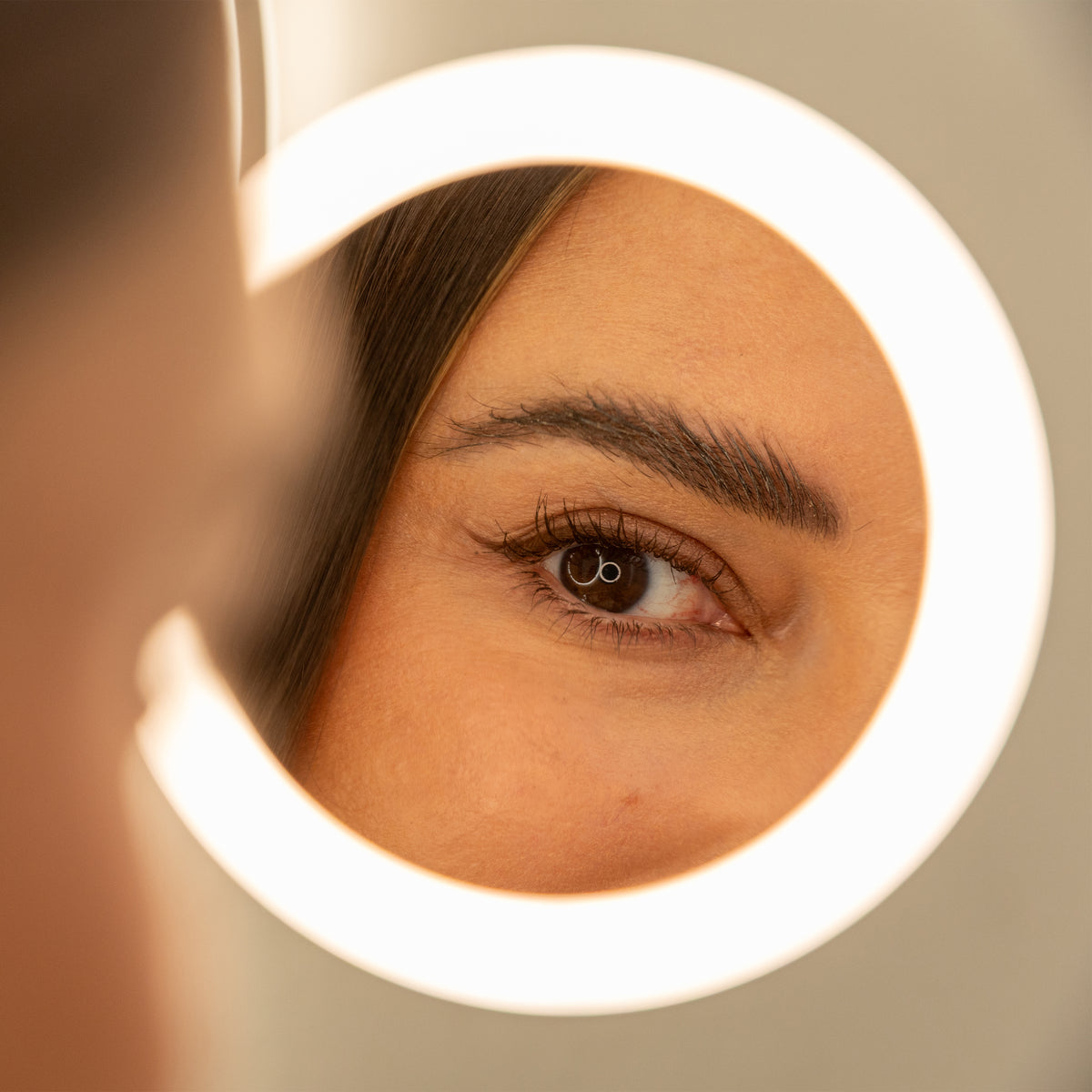 A woman's eye is reflected in the Artika Radia 9 in. Cordless LED Cosmetic Mirror, glowing with soft, warm light.