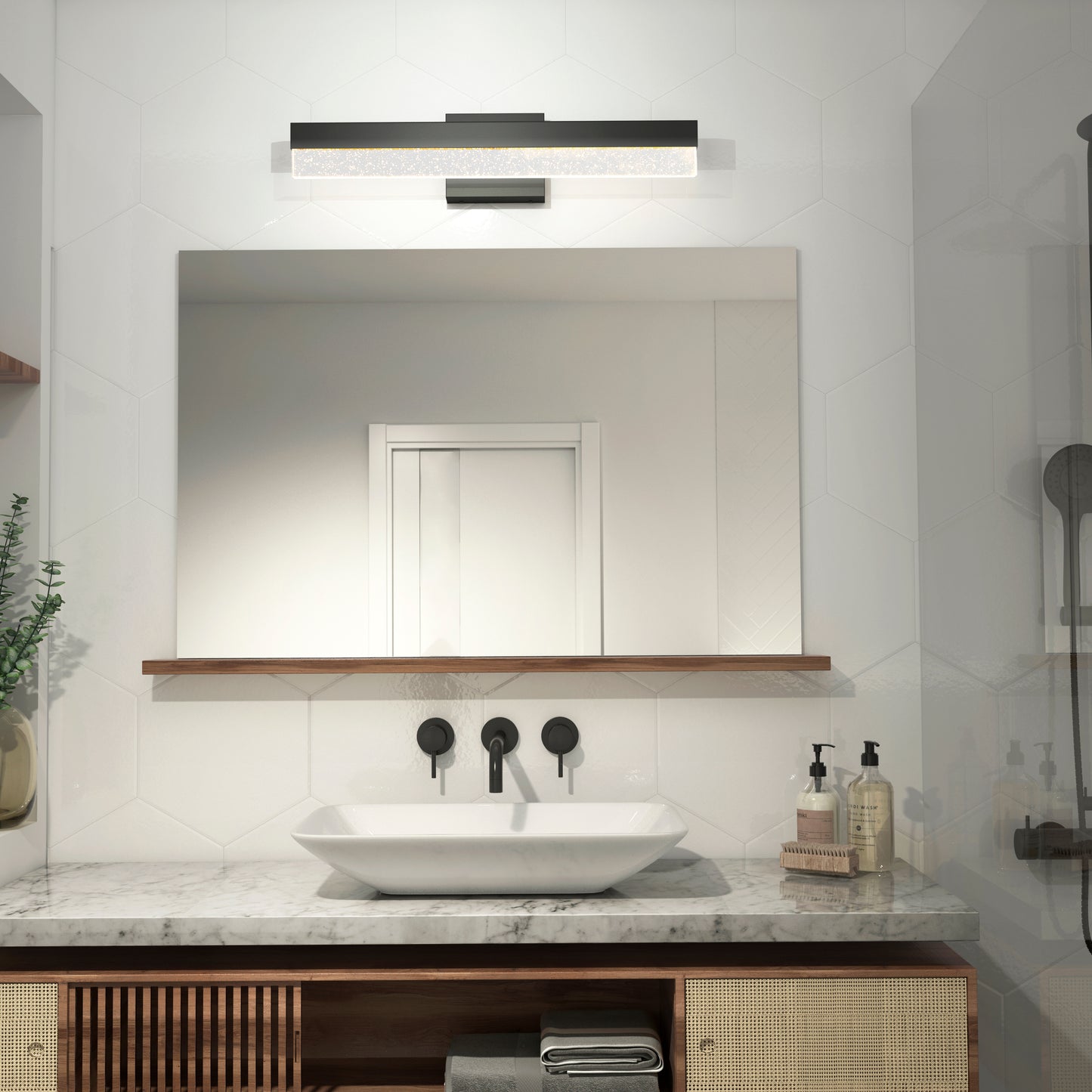 A modern bathroom features a large mirror, vessel sink on a marble countertop, black wall-mounted faucet, soap dispensers, folded towels, and a small plant on a wooden shelf. Above the mirror is the Artika Bubble Bar LED bathroom vanity light.