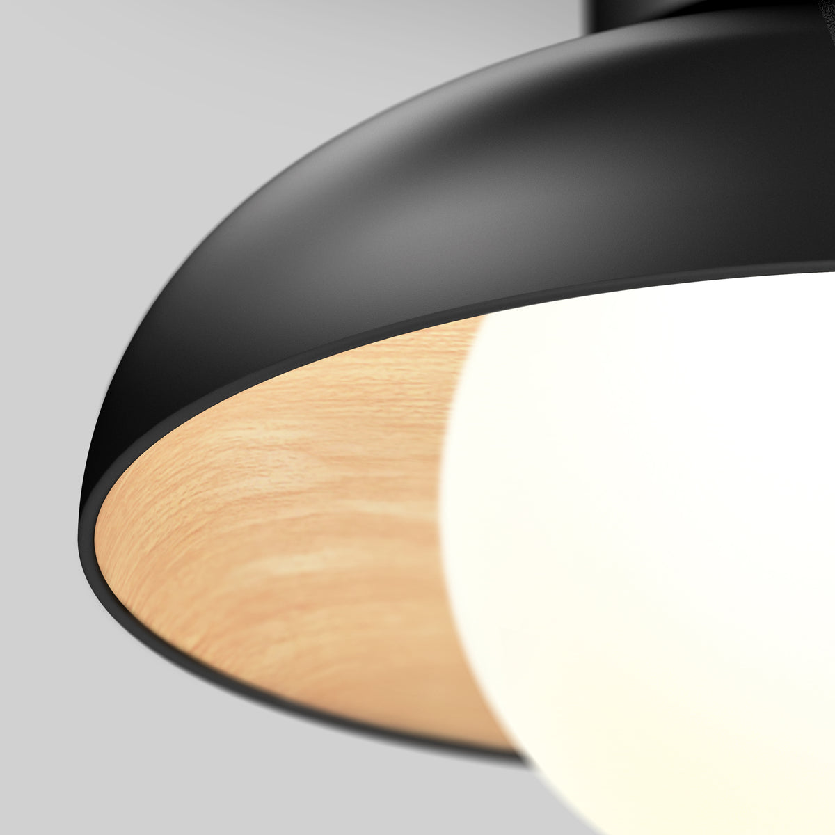 Close-up of a modern pendant lamp featuring a black metal exterior, a wood-textured inner lining, and a glowing white light bulb, set against a plain light gray background.