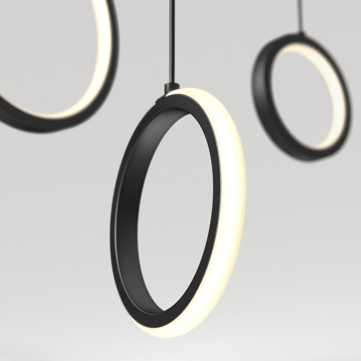 Close-up of modern, circular pendant lights with black frames and glowing white edges, suspended against a plain, light background. The focus is on the illuminated rings, creating a minimal and contemporary look.