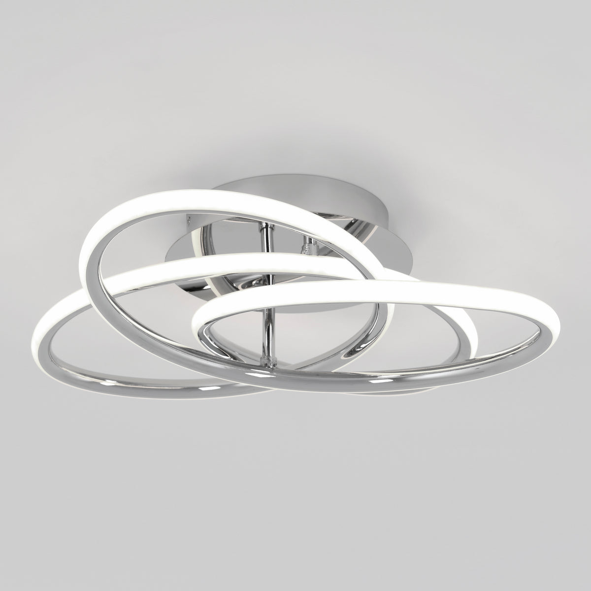 A modern ceiling light fixture with two intertwined, illuminated LED rings in a chrome finish, mounted on a round base against a plain light gray background.
