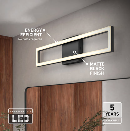 The Artika Dover modern LED bathroom vanity light 5 CCT, shown in matte black above a mirror, is energy-efficient, requires no bulbs, and includes a 5-year warranty. A plant and wood wall accents are visible below.