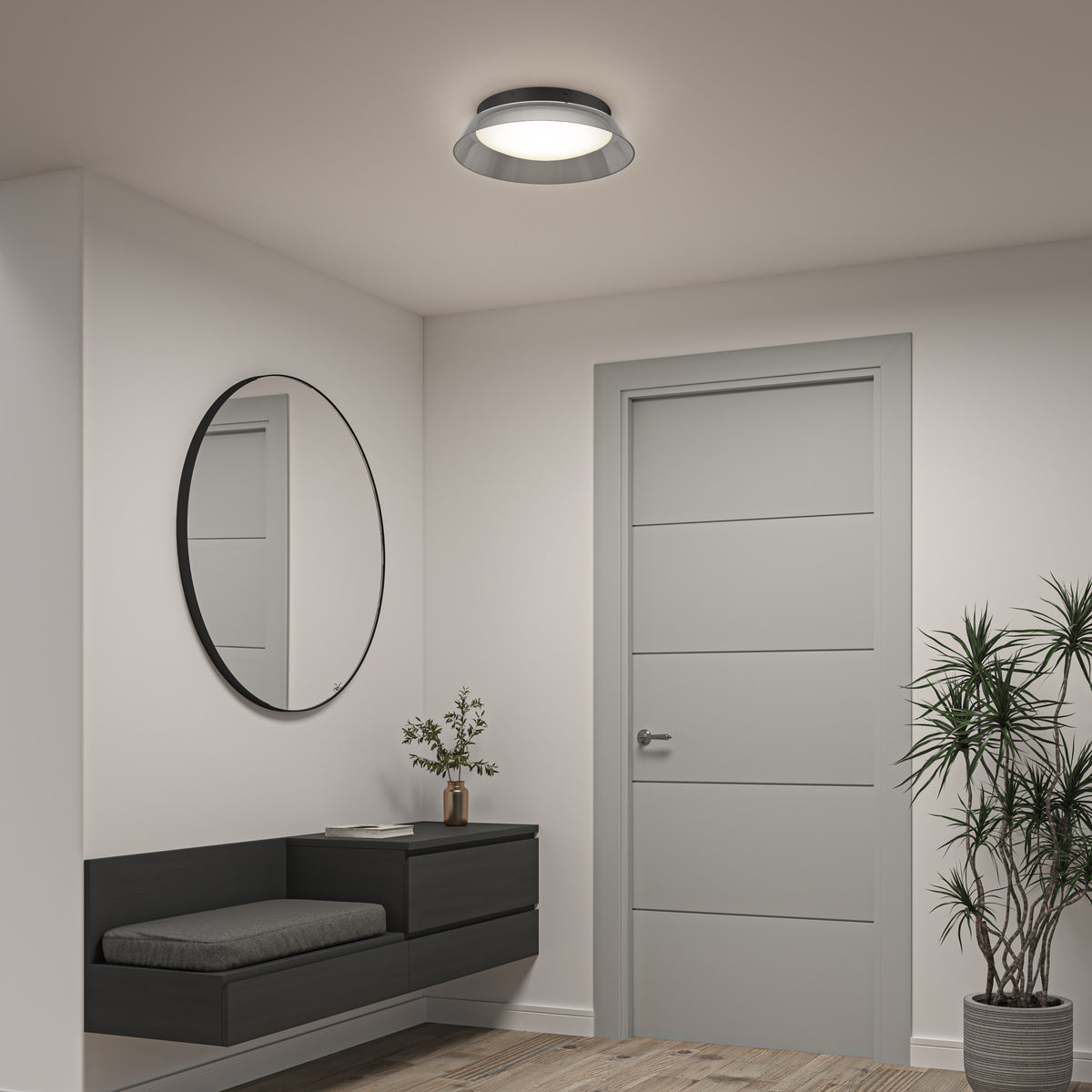 A modern hallway with light gray walls, a round mirror above a black floating bench, a small plant on the bench, a gray door, a potted plant in the corner, and a ceiling light fixture.