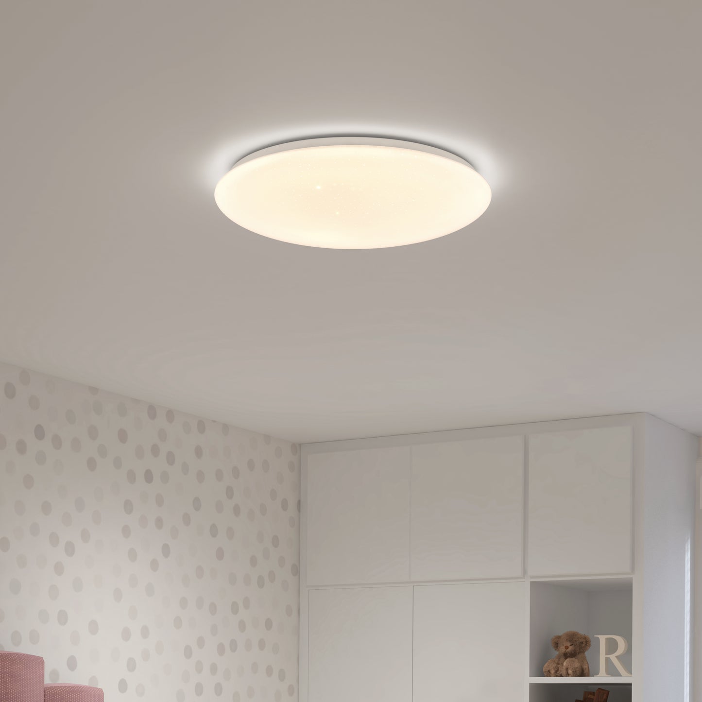 The Artika Empress 13 in. LED modern flush mount light brightens a room with polka dot wallpaper, white cabinets, and shelves displaying a small teddy bear and decor.
