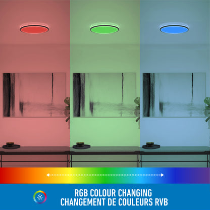 A room illuminated by the Artika Macy 15 in. LED modern flush mount light RGB Wifi shows sections in red, green, and blue. The text RGB Colour Changing / Changement de Couleurs RVB appears above a multicolor gradient bar.
