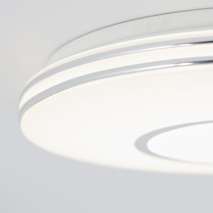 Close-up of the Artika Horizon 13 in. LED flush mount light 3 CCT—modern and circular with a smooth white surface and metallic accents—illuminating softly against a plain, light-colored background.