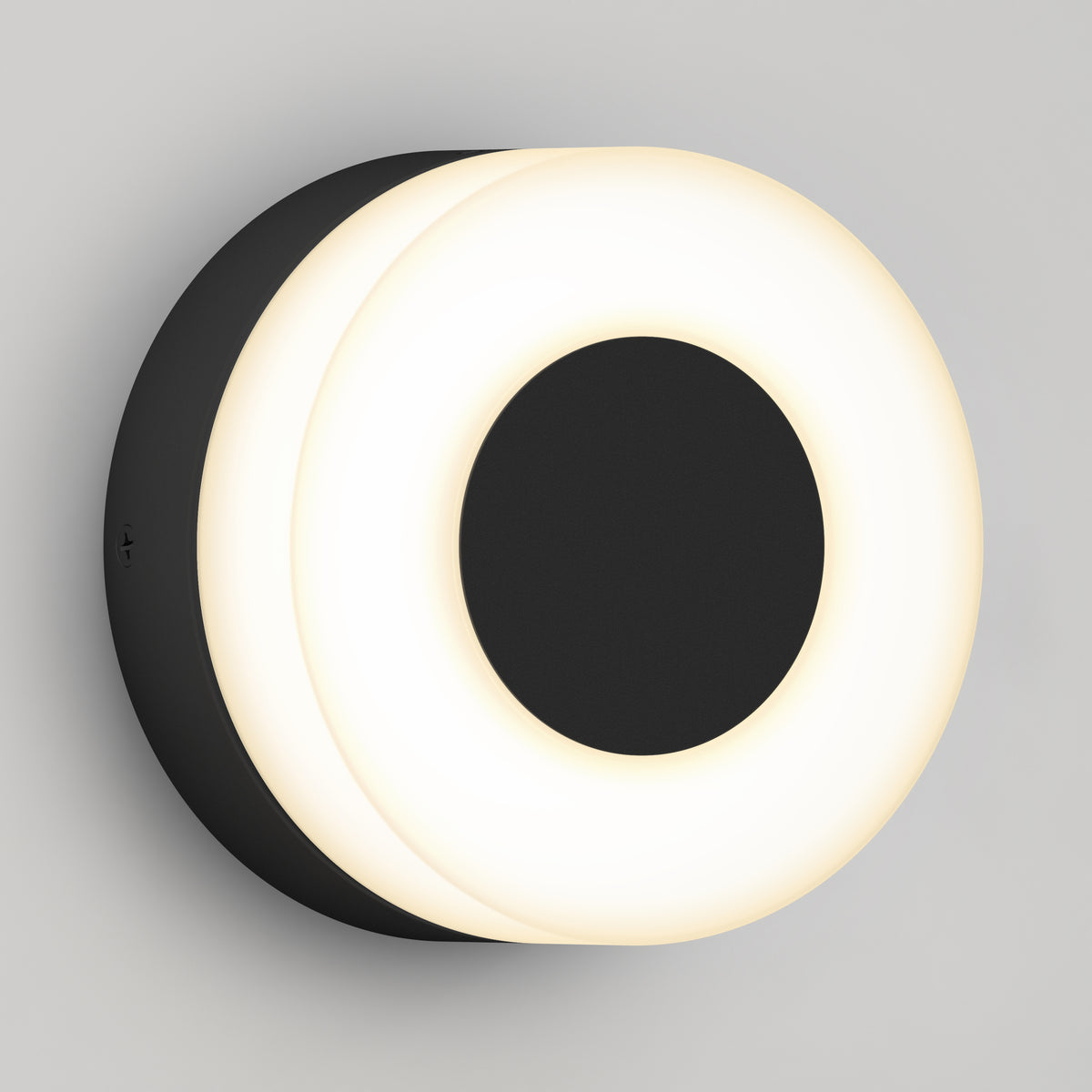 A modern wall sconce with a circular black base and a glowing white ring around a solid black center, mounted on a light gray wall.