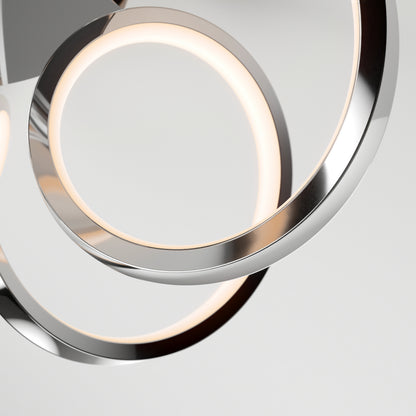 Close-up of two overlapping Swirl Ribbon LED flush mount lights by Artika, featuring sleek metallic silver frames. The dimmable fixtures emit a soft, warm glow against a plain light gray background, highlighting their modern minimalist design.