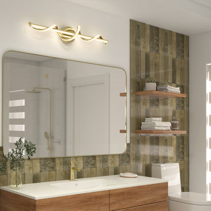 Modern bathroom with a large rectangular mirror, gold faucet, and Artika Coda modern LED bathroom vanity light 5 CCT. Greenish-brown tiles line the wall, with wooden shelves over the toilet next to a wooden vanity with a white countertop.