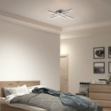 A modern bedroom with a wooden bed, gray bedding, a dresser, and a chair. There is a unique geometric ceiling light and framed photos on the wall. The room has neutral-colored walls and minimal decor.