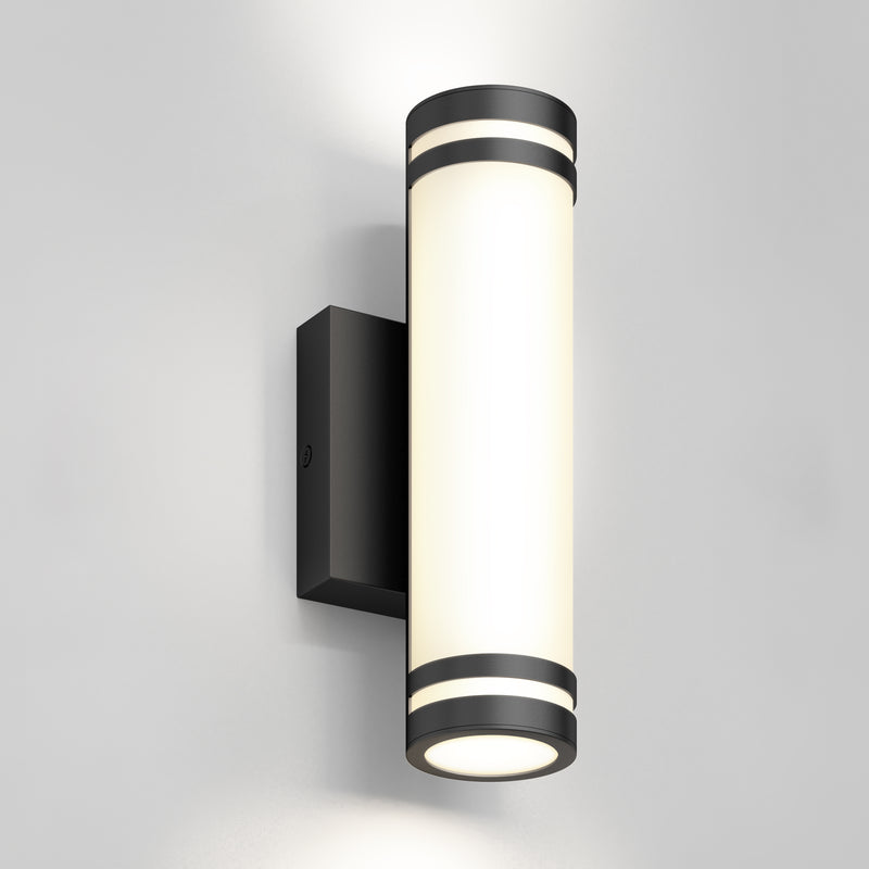 The Artika Bradley modern LED indoor-outdoor wall light 3 CCT features a black base and frosted white diffuser, mounted on a light gray wall, emitting soft upward and downward lighting.