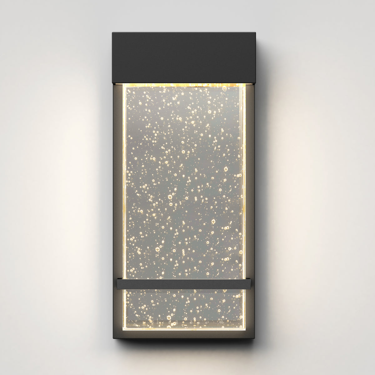 A modern rectangular wall sconce with a dark frame, featuring an illuminated glass panel filled with small bubbles, mounted on a light gray wall.