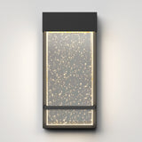 A modern rectangular wall sconce with a dark frame, featuring an illuminated glass panel filled with small bubbles, mounted on a light gray wall.