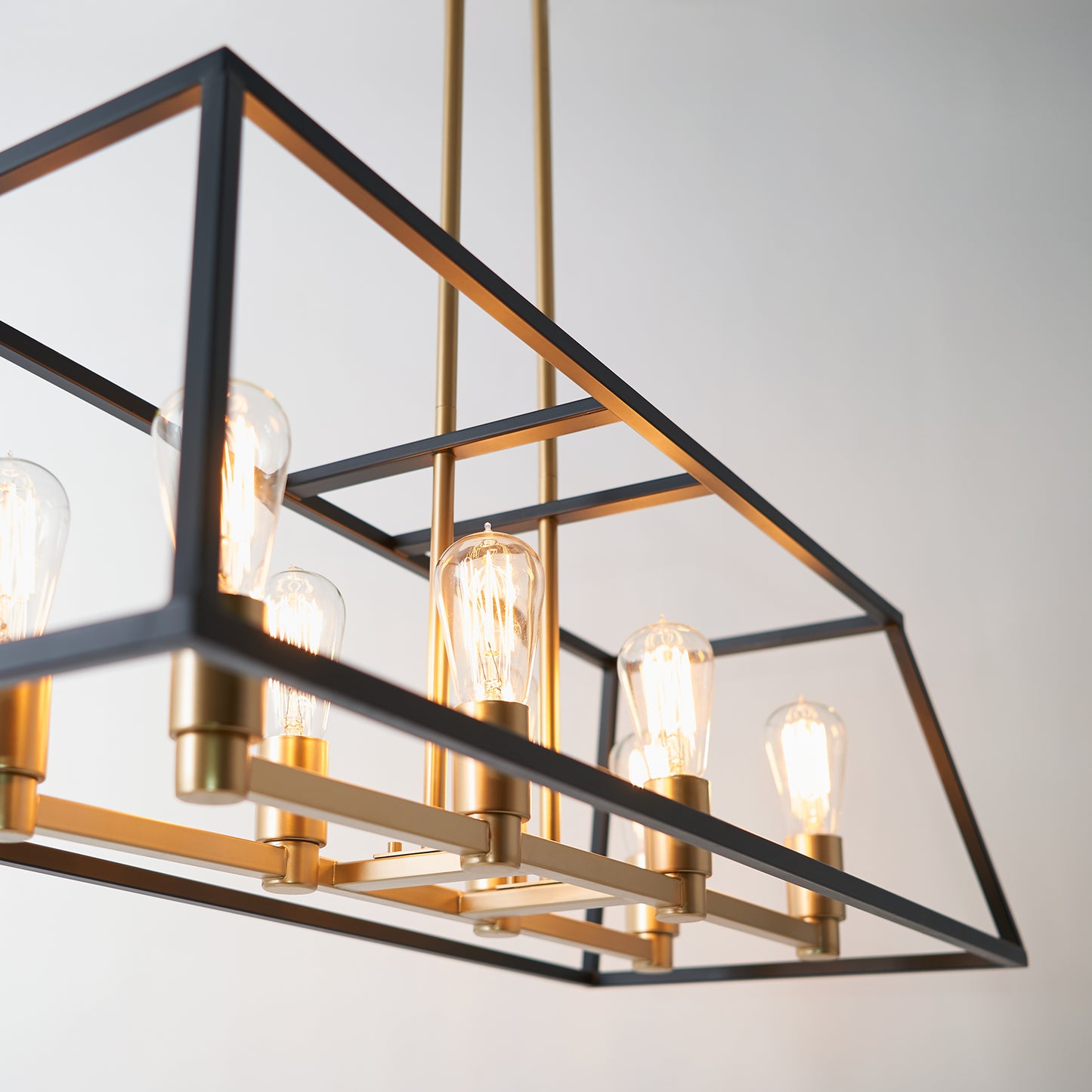 The Carter Long 8-light Chandelier by Artika features exposed bulbs and a black and gold metal frame, suspended from the ceiling against a plain light background.