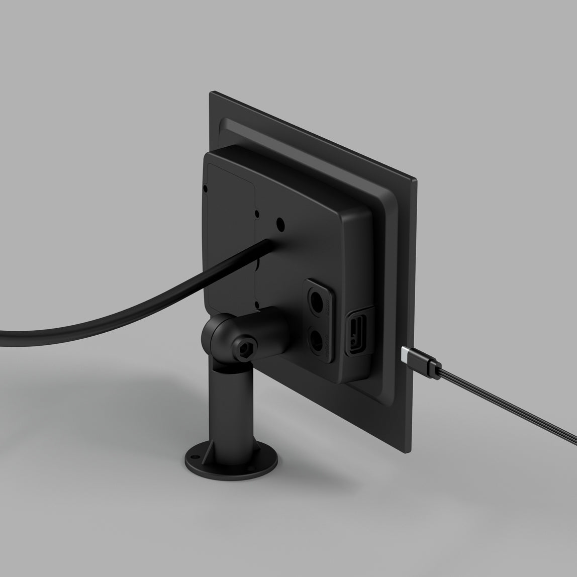 A black electronic device is mounted on a stand, viewed from the back. Two cables are connected to the device: one thick cable and one thin cable, both plugged into separate ports. The background is plain gray.