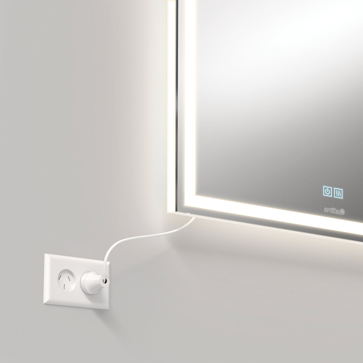 A close-up of a wall-mounted mirror with LED lights around its edge. A white power cord is plugged into a nearby wall socket below the mirror. The mirror displays faint touch controls on its surface.