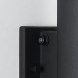 Close-up of a black, wall-mounted electronic device with a round button and a knob, positioned against a white wall. The surface of the device has a matte, textured finish.
