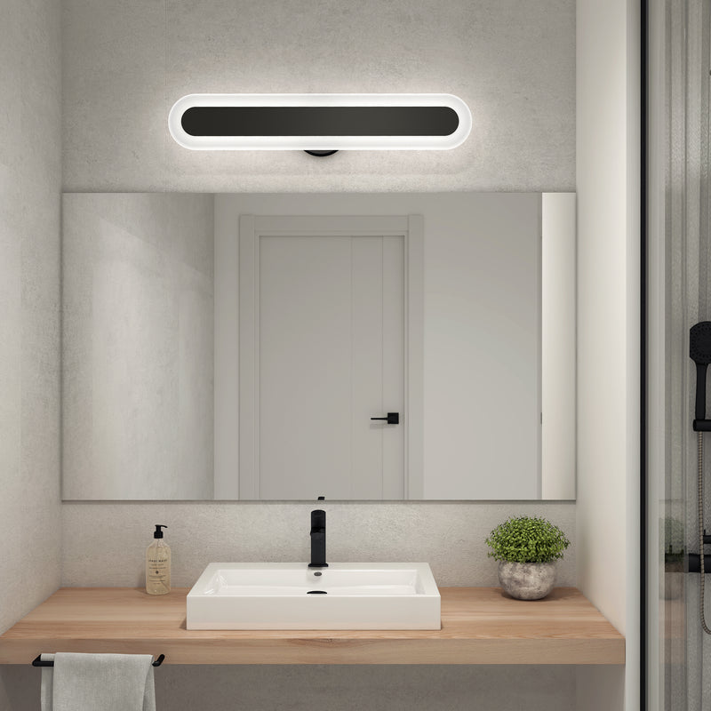 A modern bathroom features a rectangular mirror above a wooden countertop with a white sink, black faucet, soap dispenser, potted plant, and towel; an Artika Pista 27-in Integrated LED 5-CCT Vanity Light Bar is mounted above the mirror.