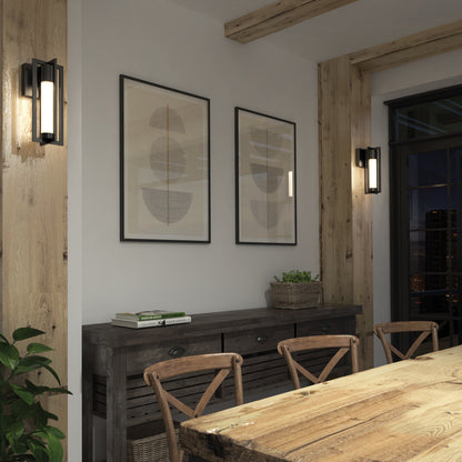 A cozy dining room with a rustic wooden table, chairs, a sideboard with books and a plant basket, two framed abstract art prints on the wall, and modern Walt indoor-outdoor LED wall lights by Artika for lighting.