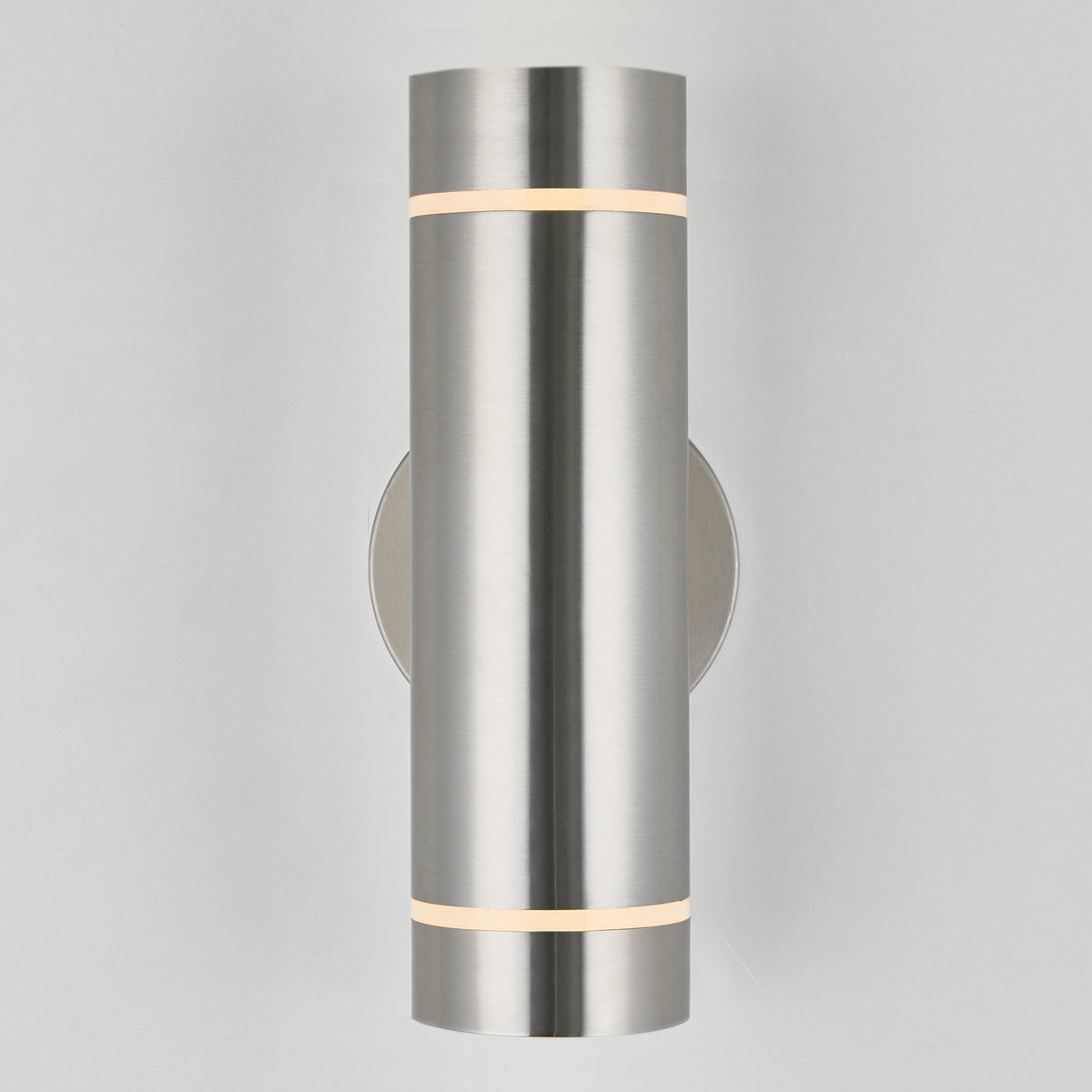 The Artika C7 indoor-outdoor wall light is a modern, rustproof cylindrical fixture in brushed metal with subtle top and bottom light bands, mounted on a plain light-colored wall—perfect for versatile indoor or outdoor use.