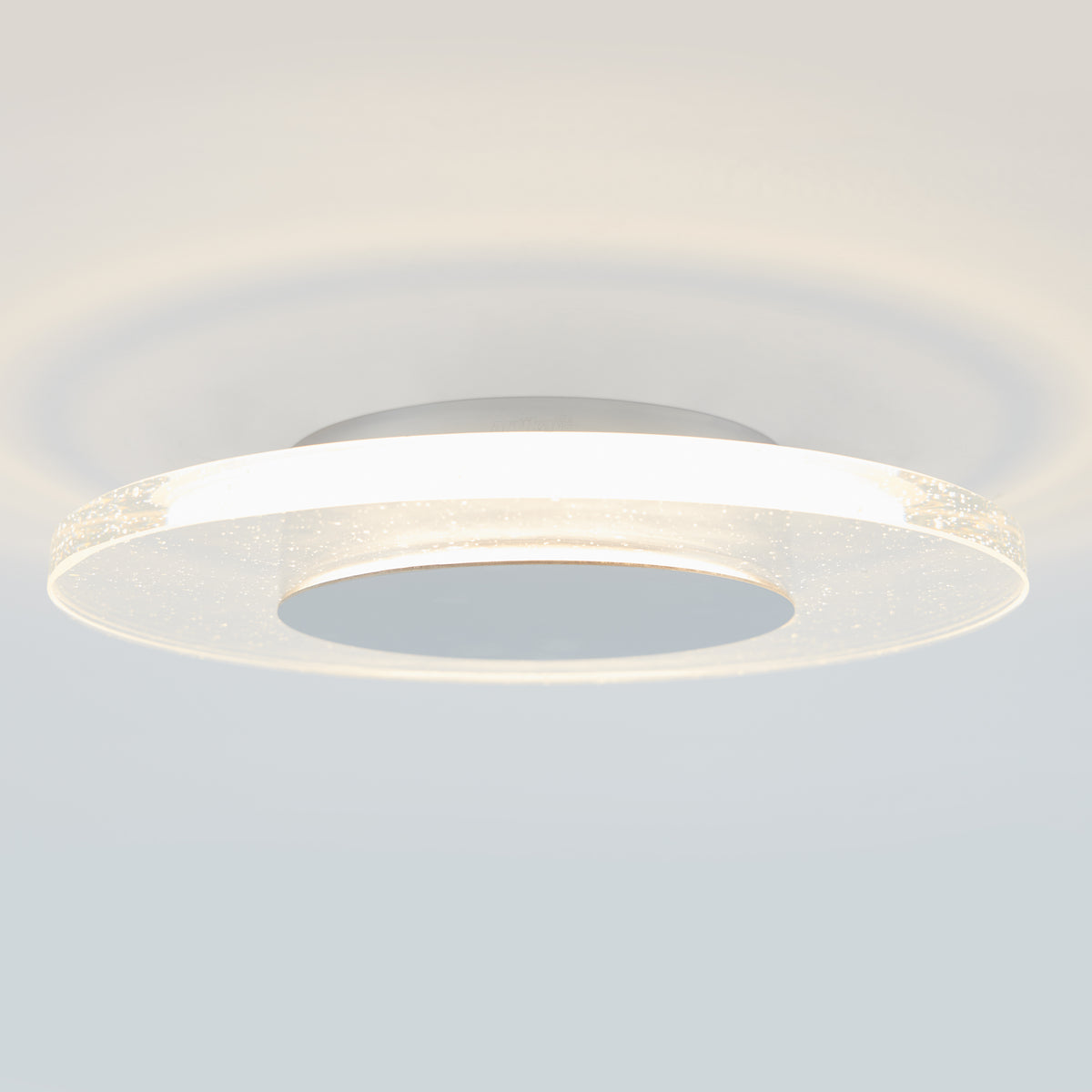 Close-up of a modern, circular ceiling light fixture with a glowing outer ring and a frosted, textured surface, mounted on a white ceiling.