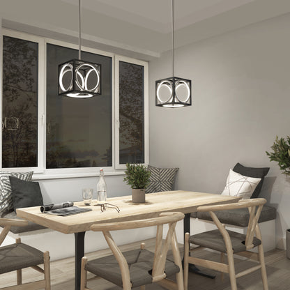 A modern dining area features a wooden table, four chairs, and the Artika Astoria LED modern pendant light in black and gold. Cushions and simple decor create a cozy vibe, with a window framing dusk-lit trees and a potted plant for freshness.